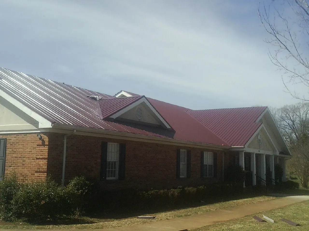 Red metal roof with gabled entries on a long brick building, from a Hail Damage Roof Repair job in Willow Street