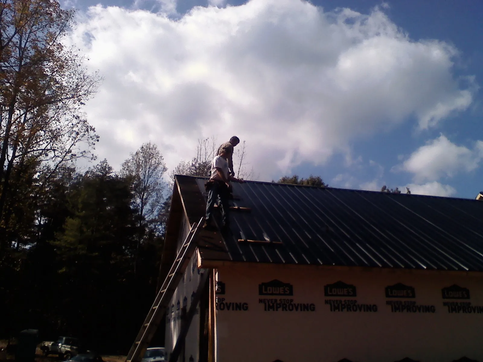 Roofer fastening dark metal panels high against a cloudy sky, from a Roof Inspection job in Willow Street