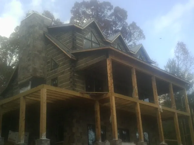 Stone chimney and dormers on a large log home with a timber porch in Willow Street