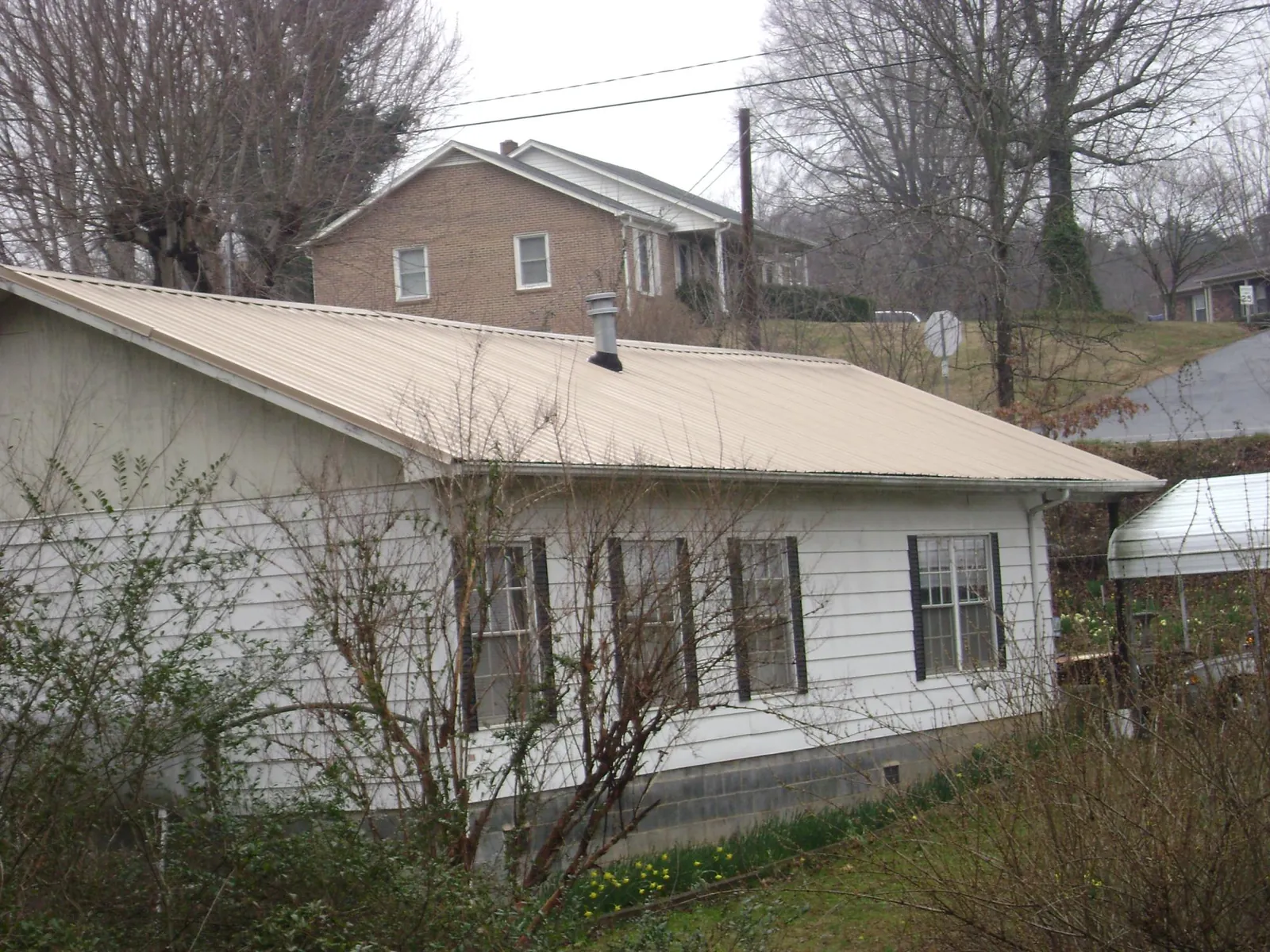 Tan metal roof on a white sided house set into a hillside — Commercial Roofing by Roofing Brothers in Willow Street